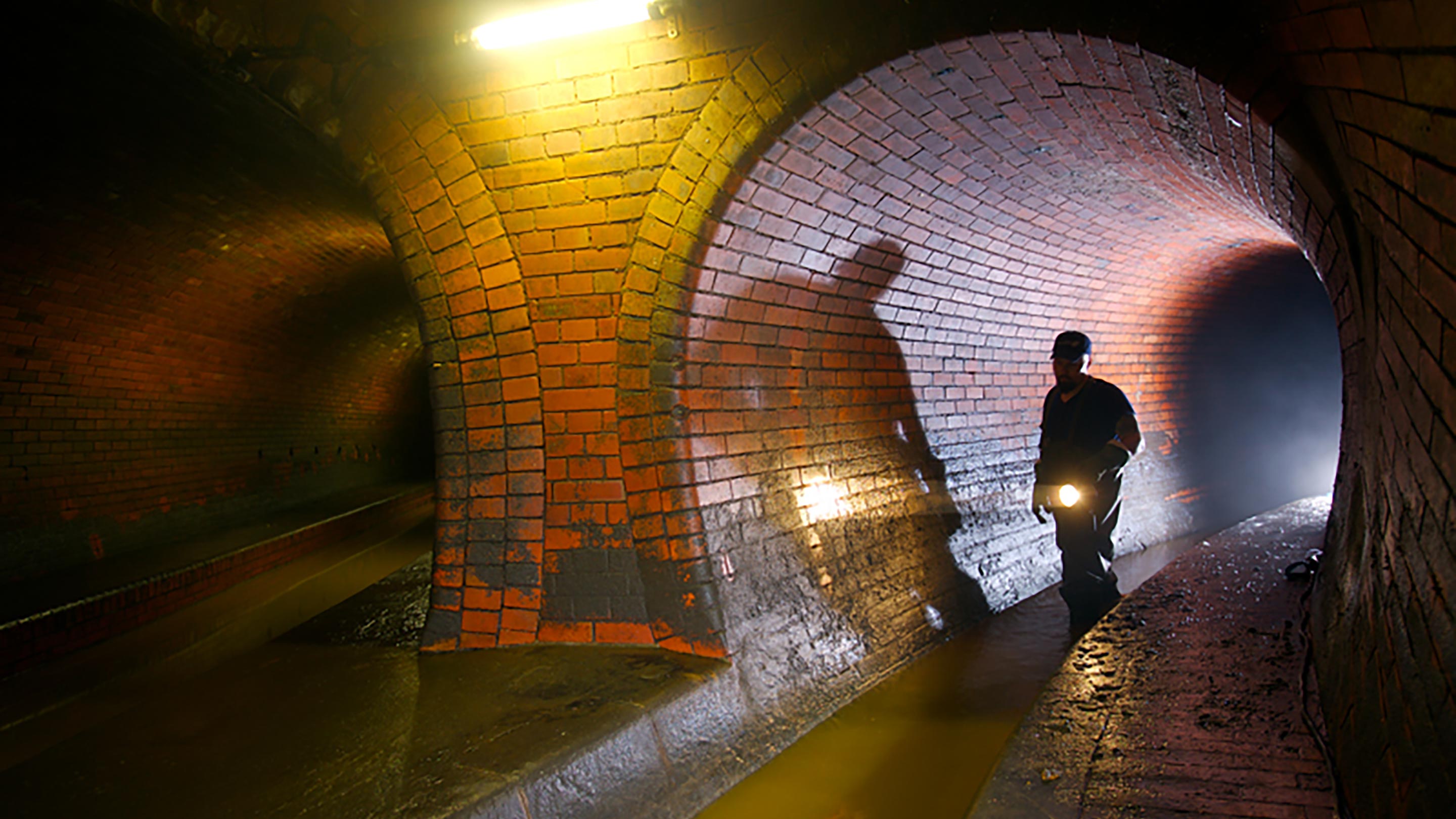 Arbeiter läuft mit Taschenlampe durch einen Abwasserkanal