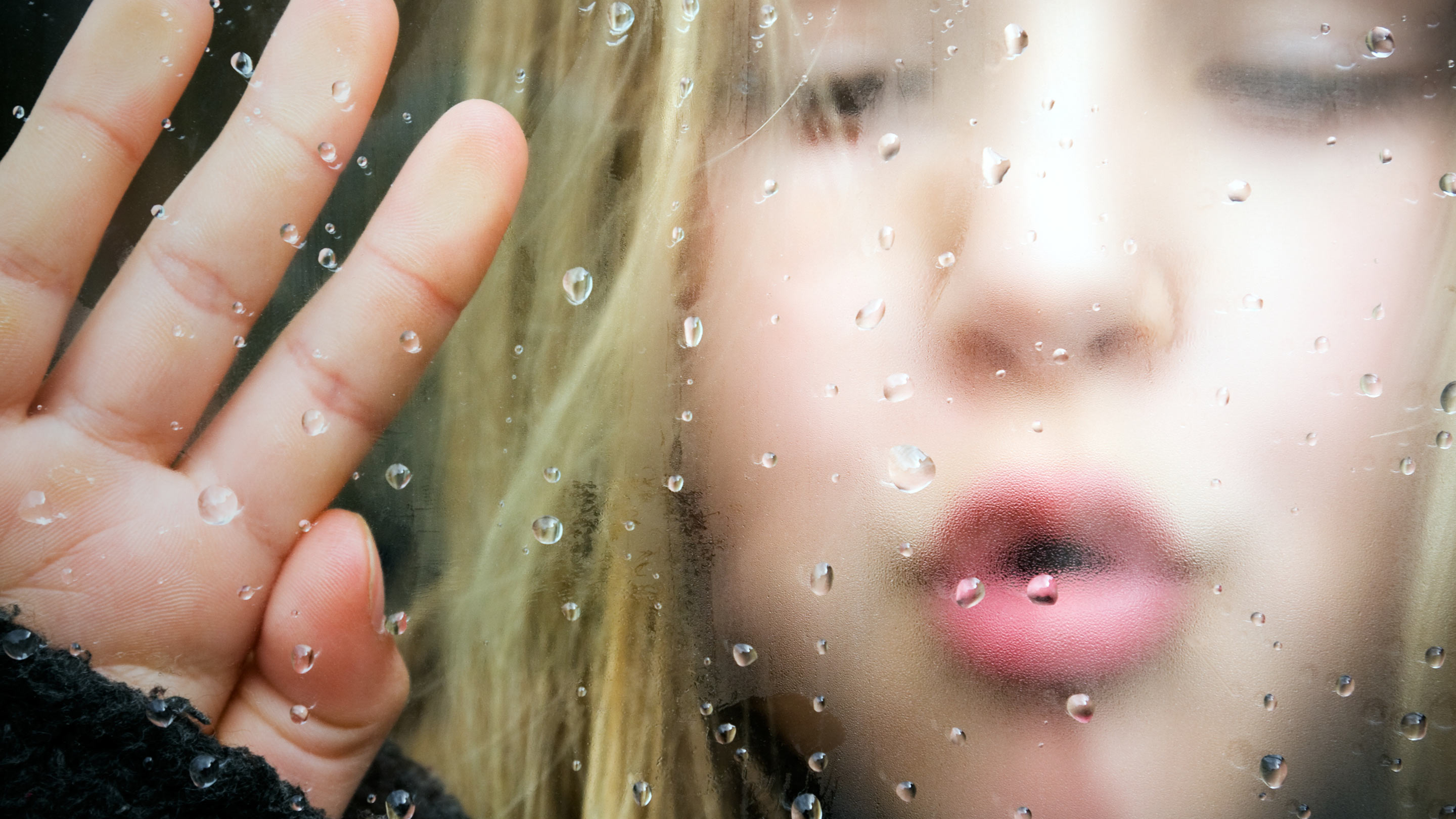 Mädchen bläst Luft gegen eine kalte Scheibe, an der Wasser kondensiert