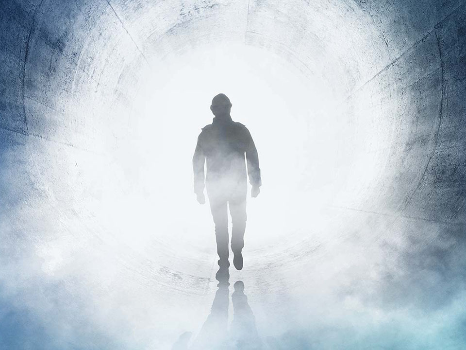 Mann läuft durch einen riesigen Tunnel. Von hinten strahlt weißes Licht, so dass man nur seine Silhouette erkennen kann.