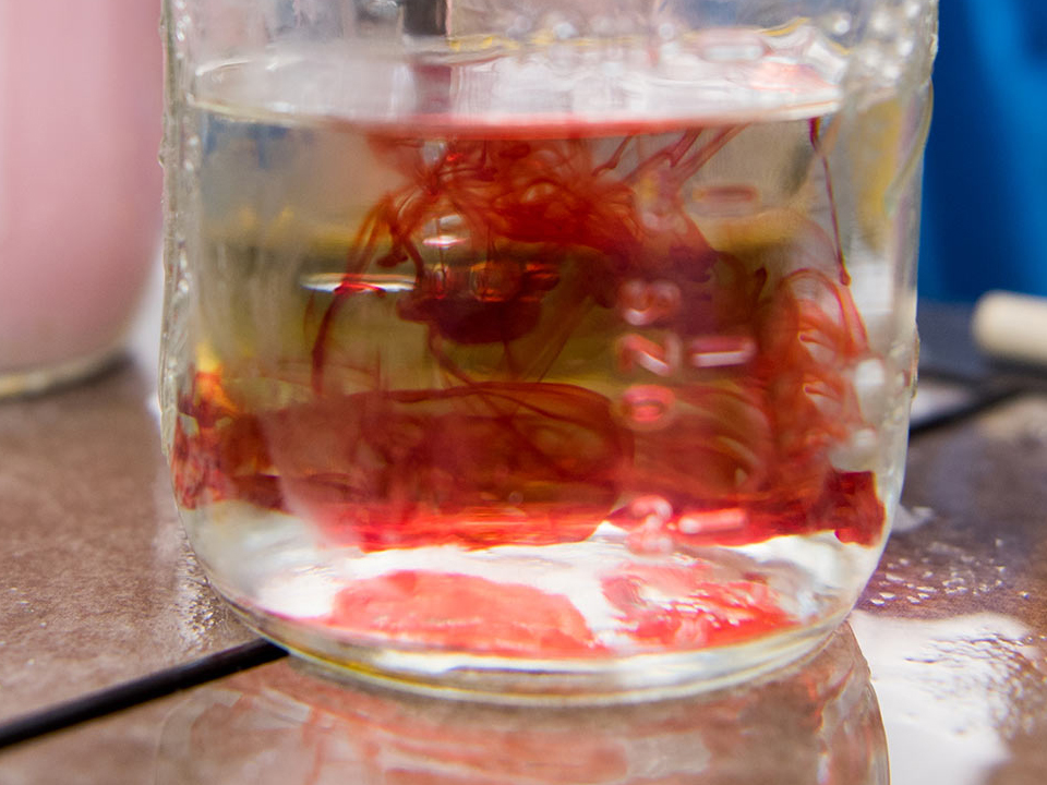 Farbige Flüssigkeit zerfließt in einem Wasserglas 